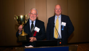 Richard Lindsey is holding the National Cotton Ginners Ginner of the Year Award. It is a large Cup.